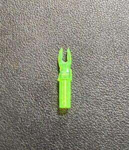 A small green plastic archery arrow nock on a textured surface.