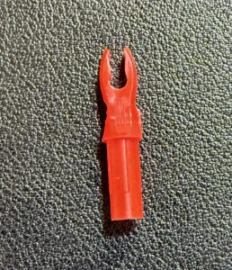 Red plastic arrow nock on a textured surface.