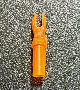 Orange plastic archery arrow nock on a textured surface.