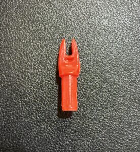 Close-up of a red plastic arrow nock on a textured surface.