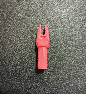 A small red plastic archery nock on a textured surface.