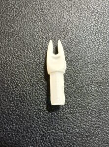 Close-up of a small white plastic fork-like tool on a textured black surface.